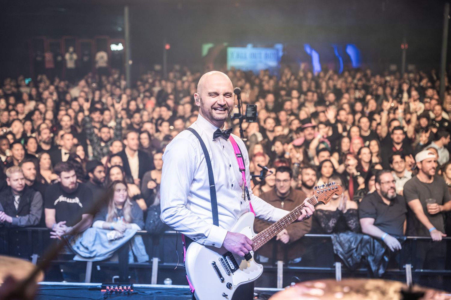 Performer playing guitar on stage with white shirt and suspenders in front of large concert crowd.