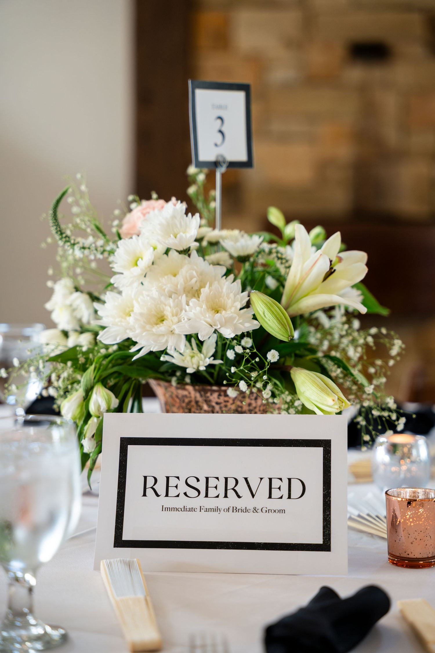 Elegant wedding table centerpiece with white lilies and daisies next to a reserved sign and table number.