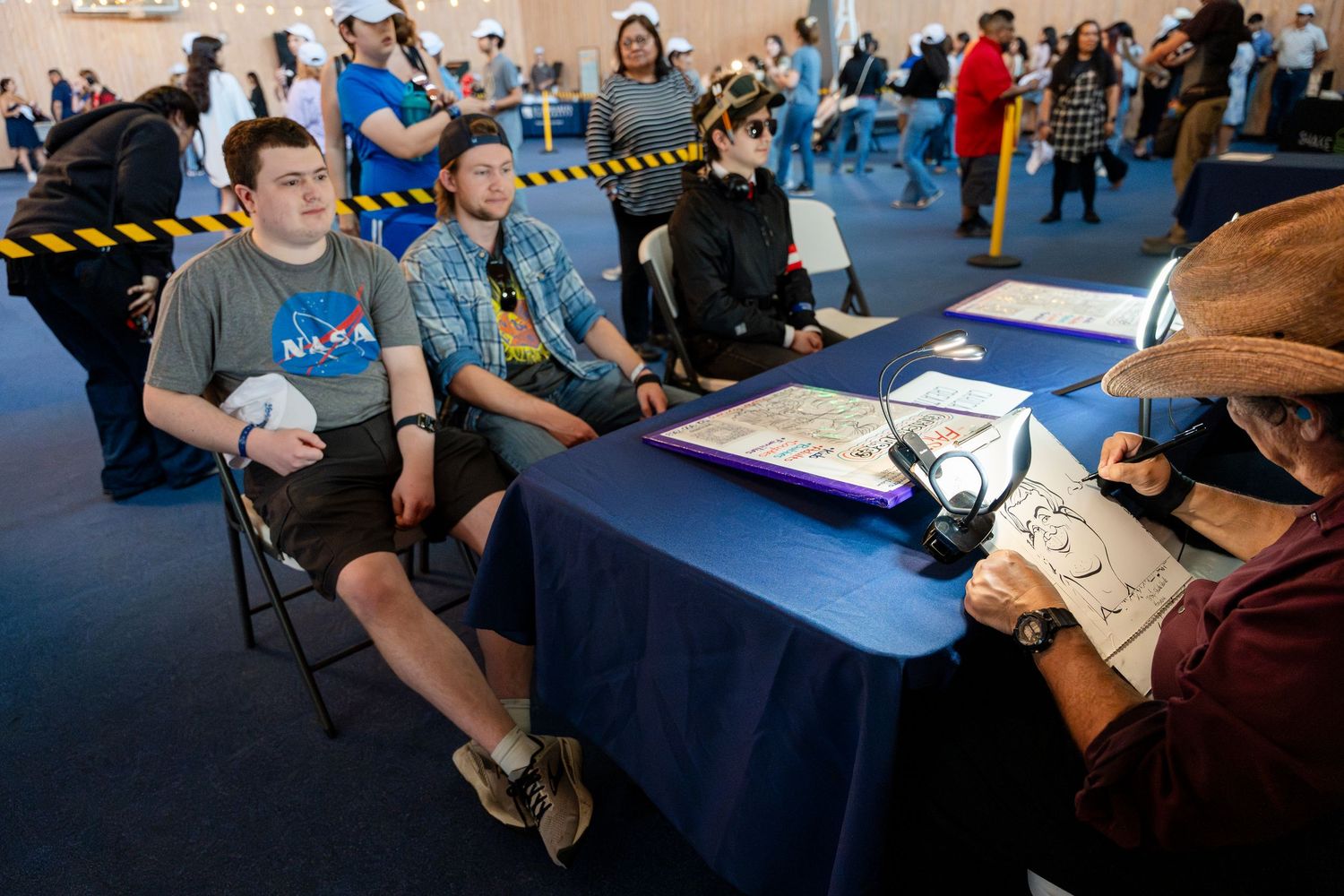 Participants sit at a table during convention signing event with NASA logos visible on their shirts.