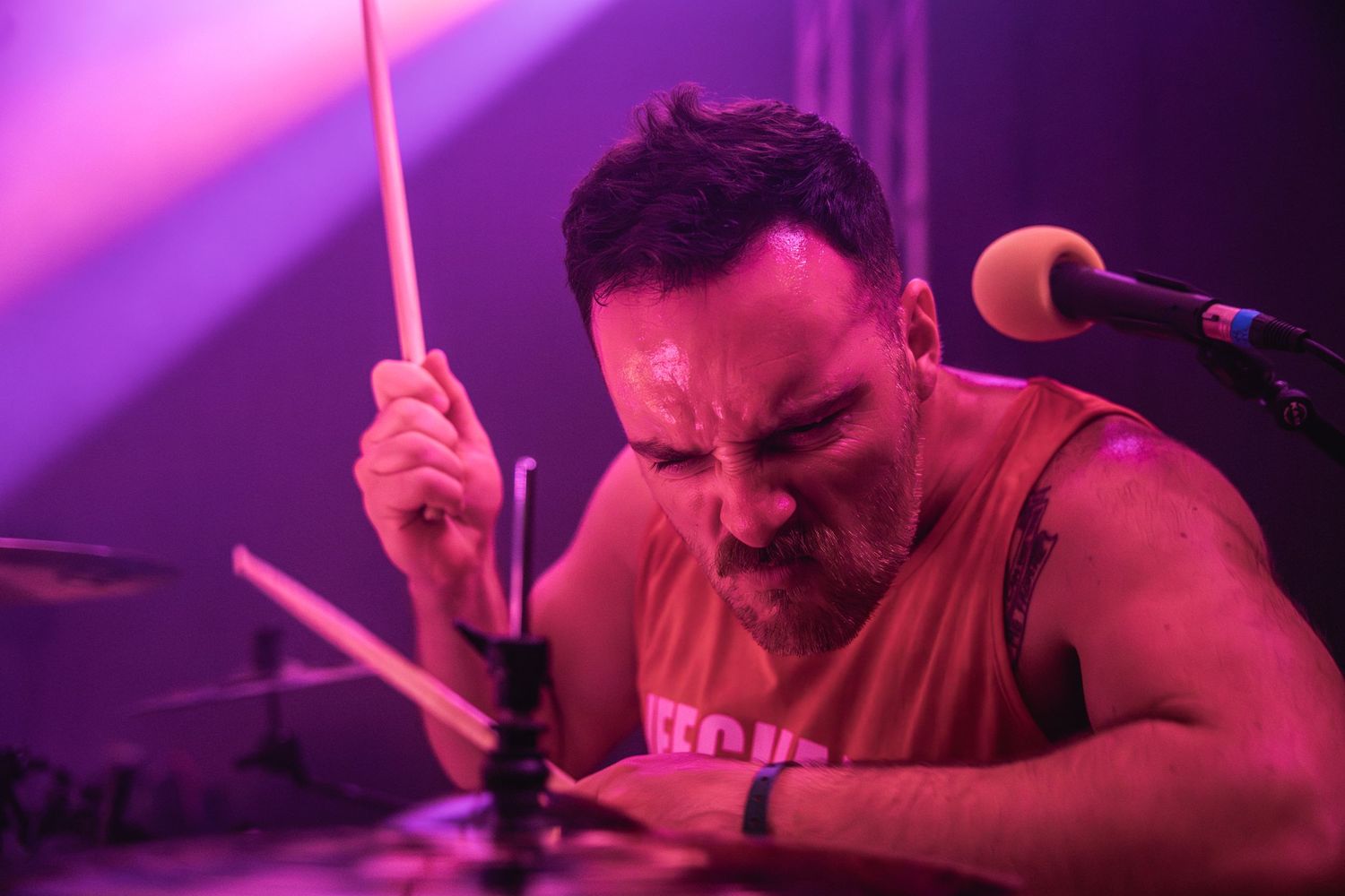 Drummer intensely plays during performance under purple stage lighting.