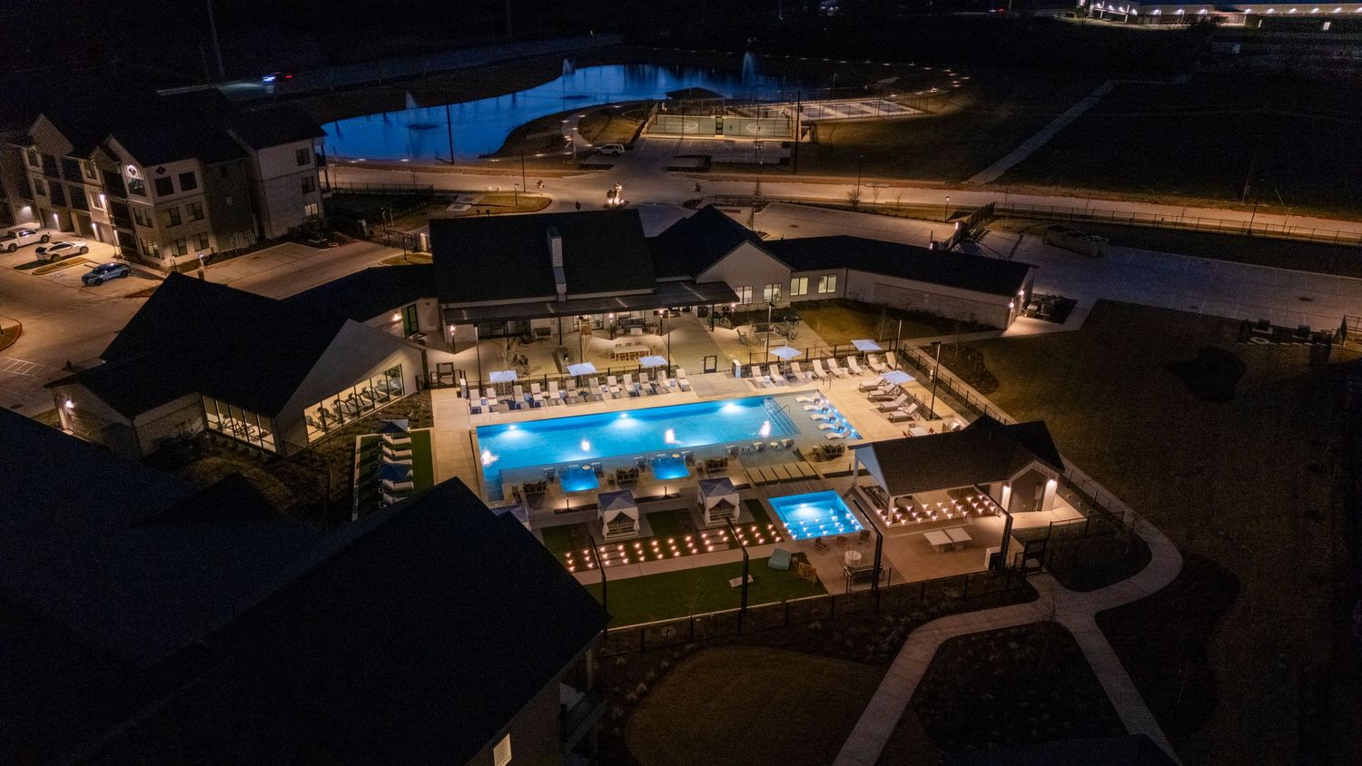 Aerial nighttime view of an illuminated resort complex with multiple swimming pools glowing bright blue against dark surroundings.