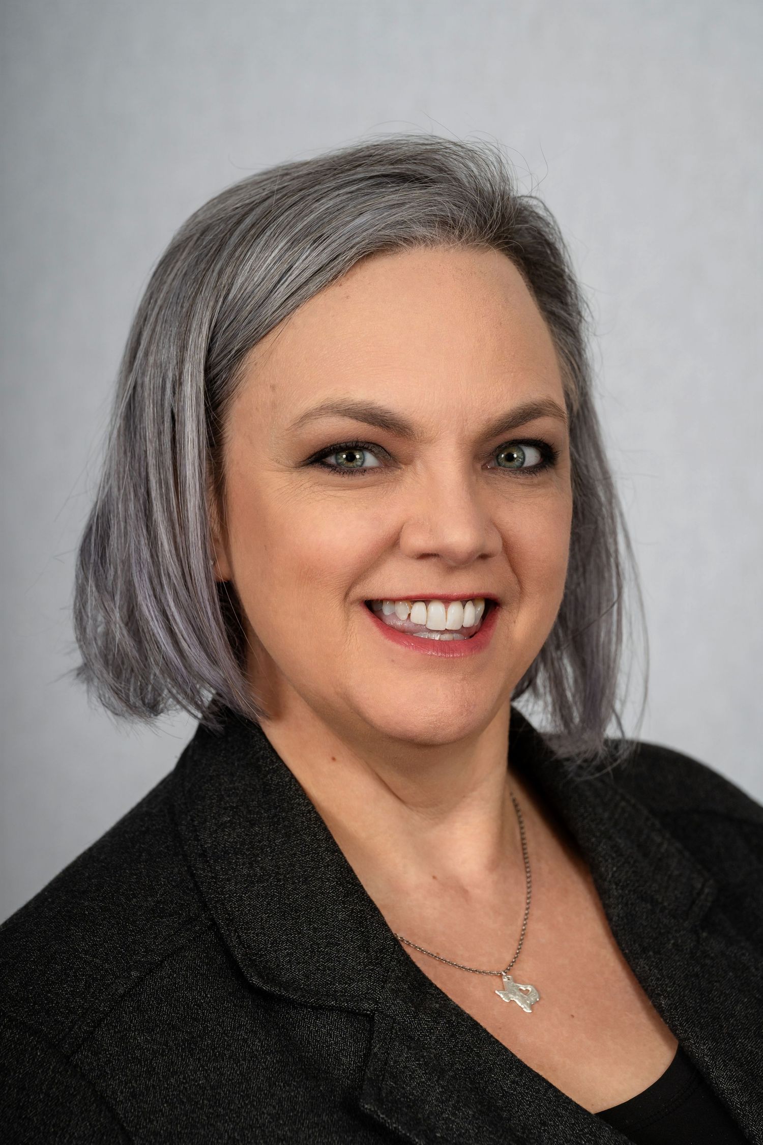 Professional headshot portrait in business attire against grey background.