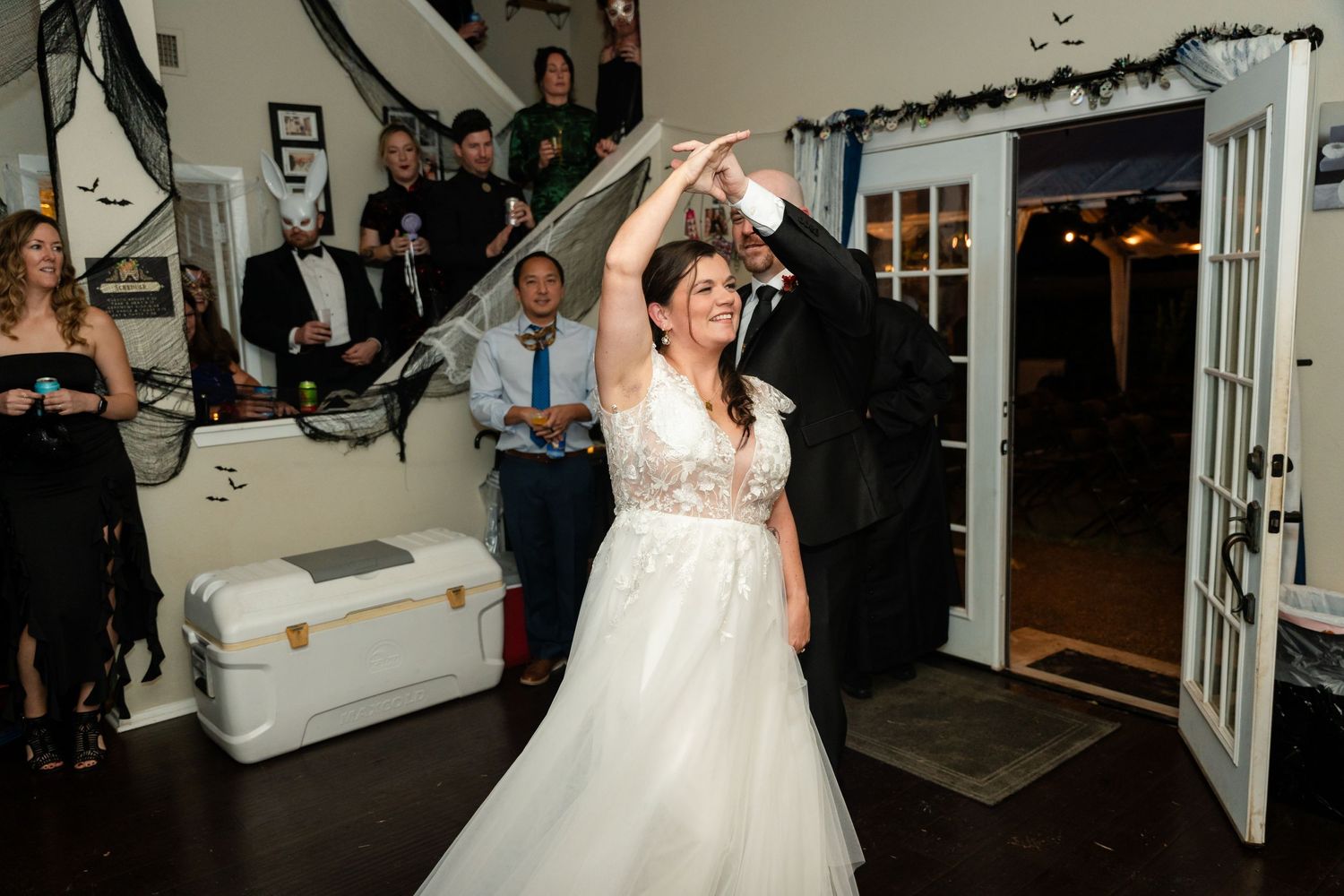 Couple dancing at indoor reception with Halloween decorations and guests watching.