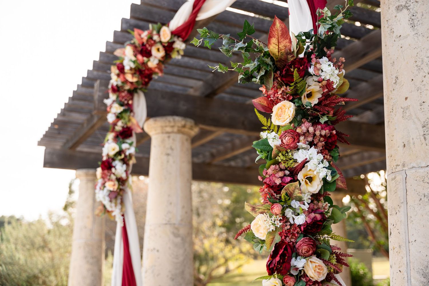 Wedding arch decorated with burgundy and cream flowers and red fabric draping.