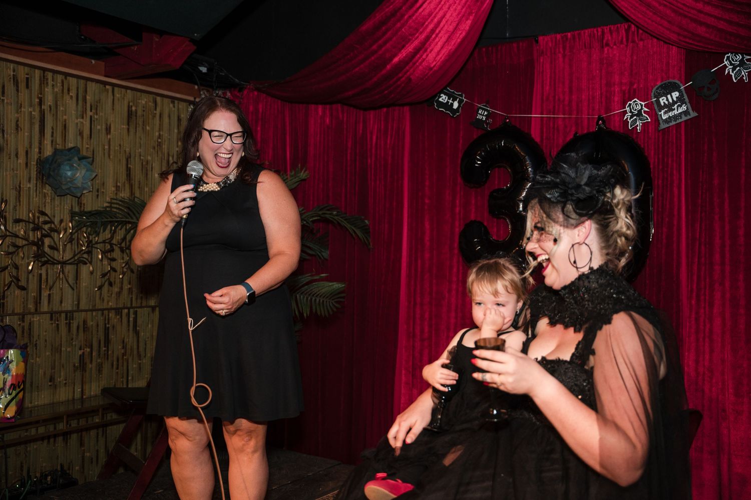 People in black attire checking their phones at a dark venue with red curtains.