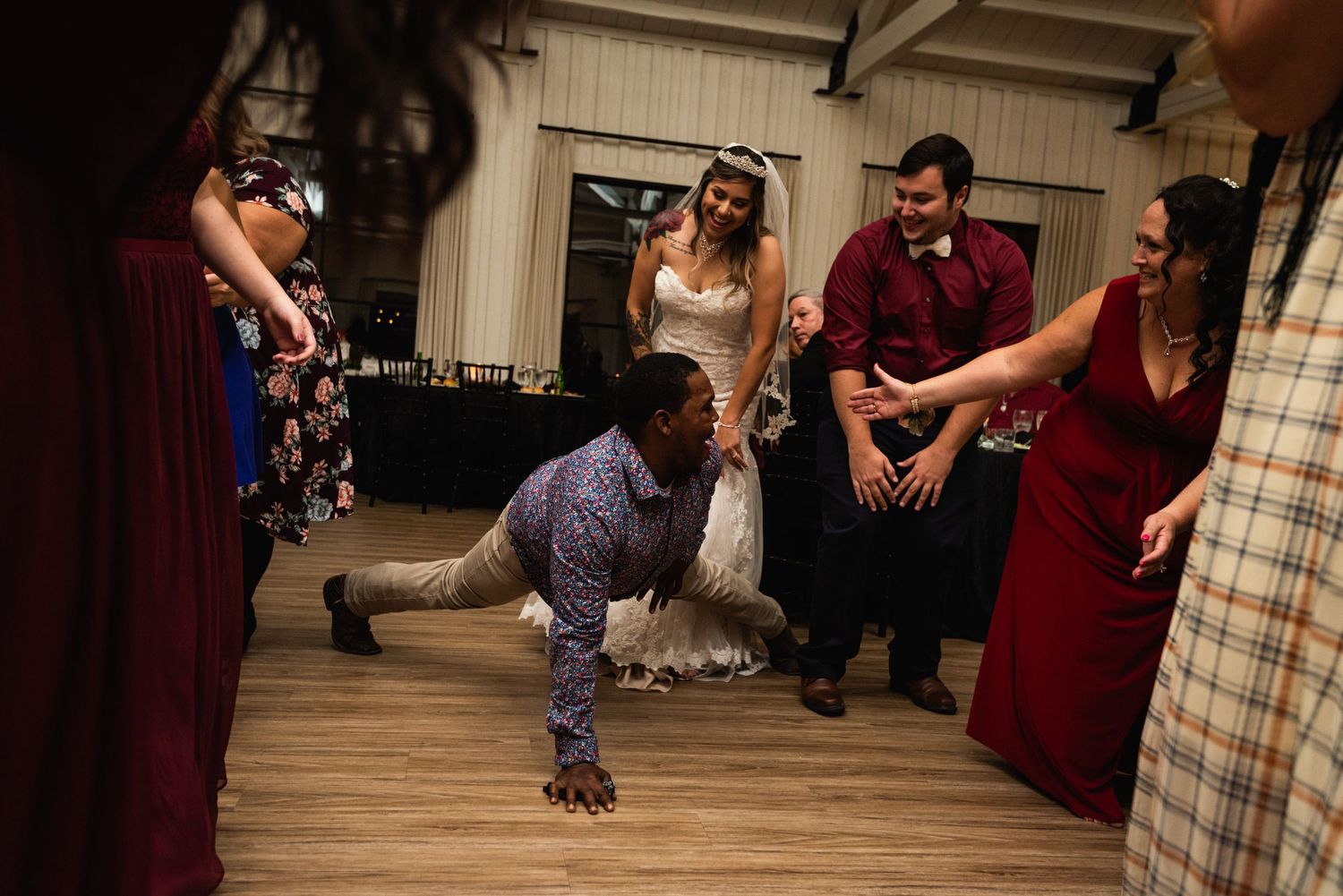 Wedding guest shows off break dancing moves on wooden floor surrounded by formal attire.