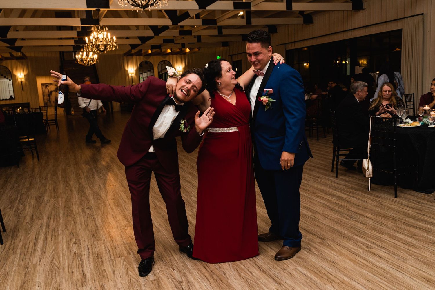Three wedding guests dancing and posing together at a reception with exposed wooden beams.