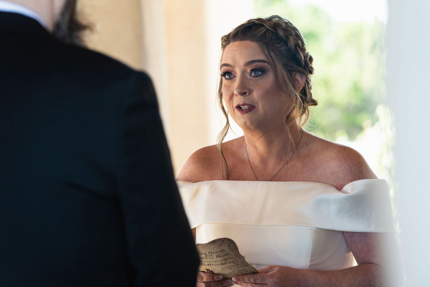 Close-up of bride in off-shoulder dress during emotional ceremony moment.
