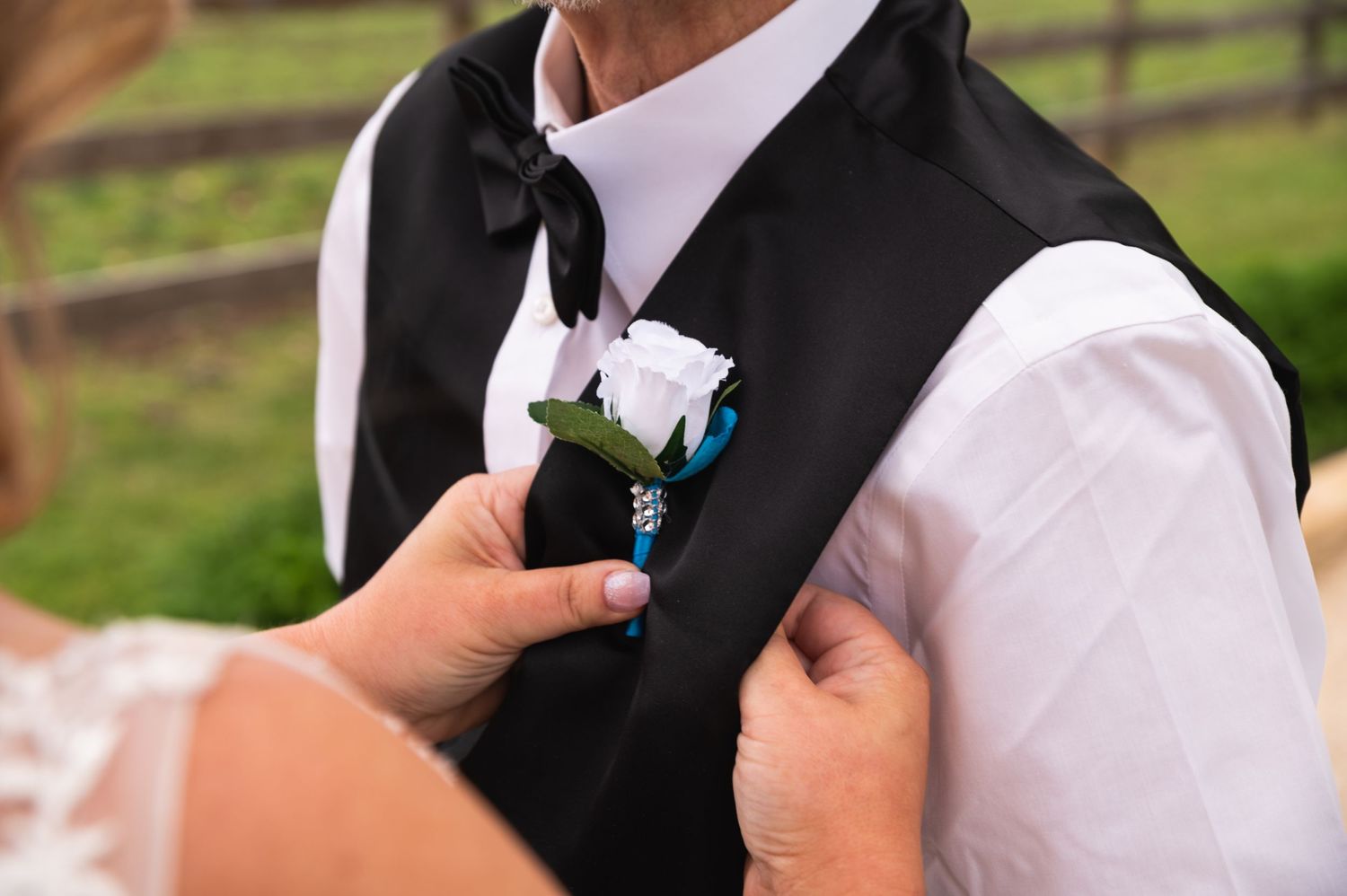 Close-up of hands pinning a white and blue boutonniere on a formal black vest.