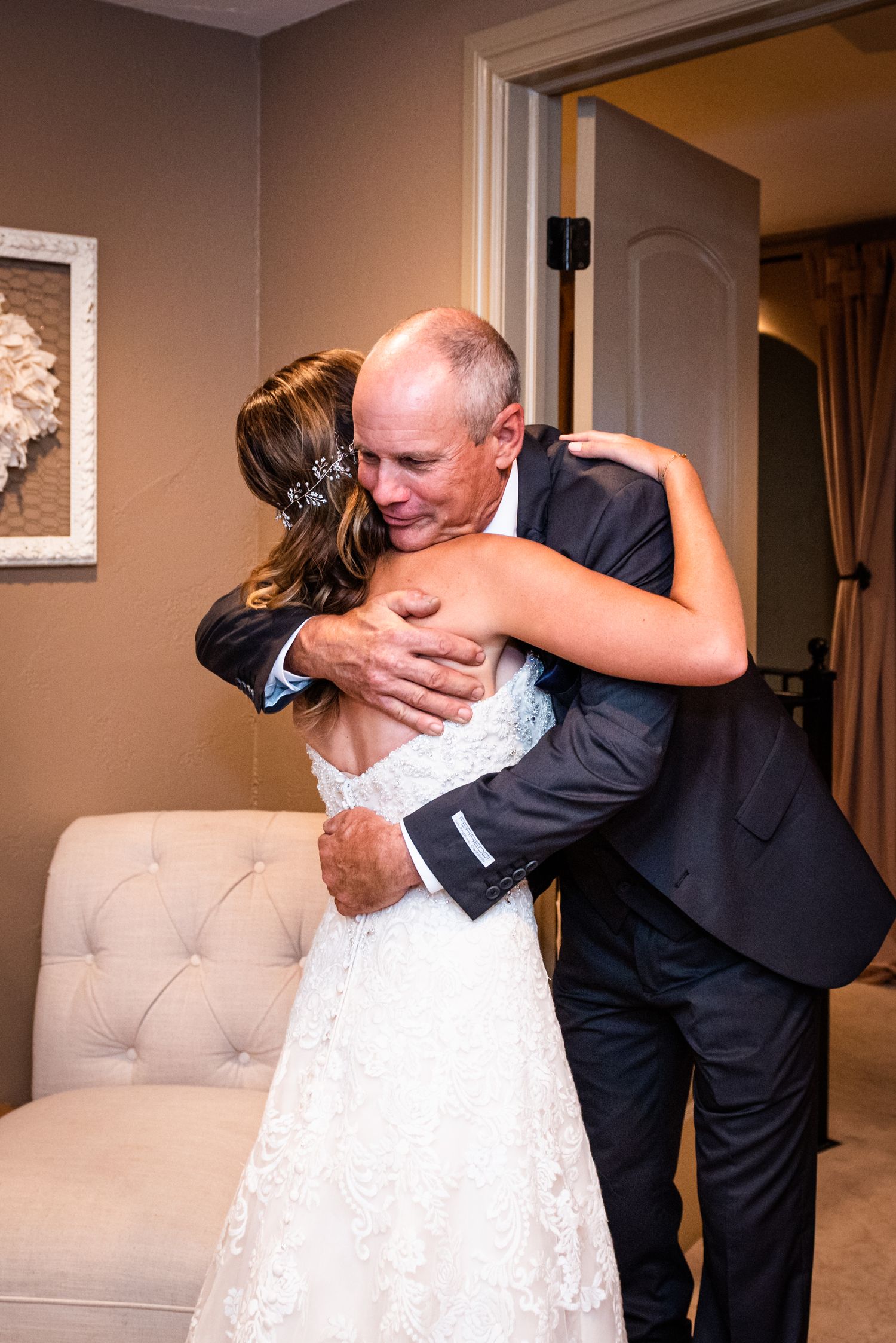An emotional embrace in formal attire against a beige interior setting.