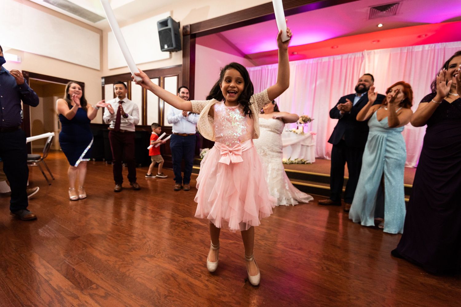 Guest in pink dress dances joyfully at wedding reception under colorful lighting.