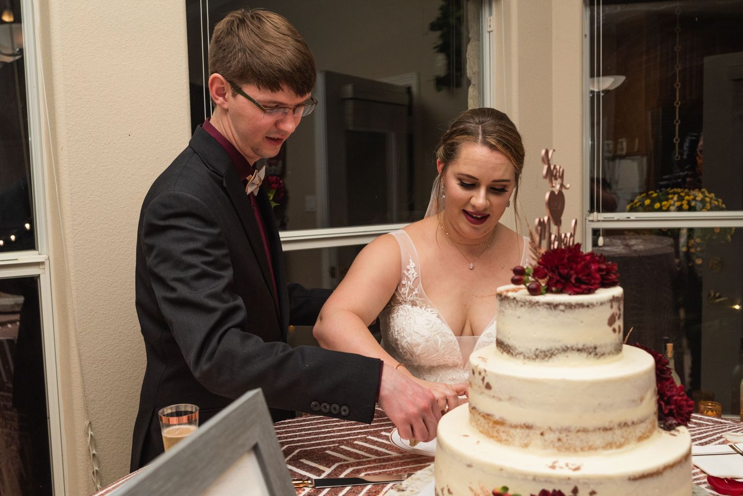 A wedding couple cuts into their elegant three-tiered white and burgundy wedding cake.