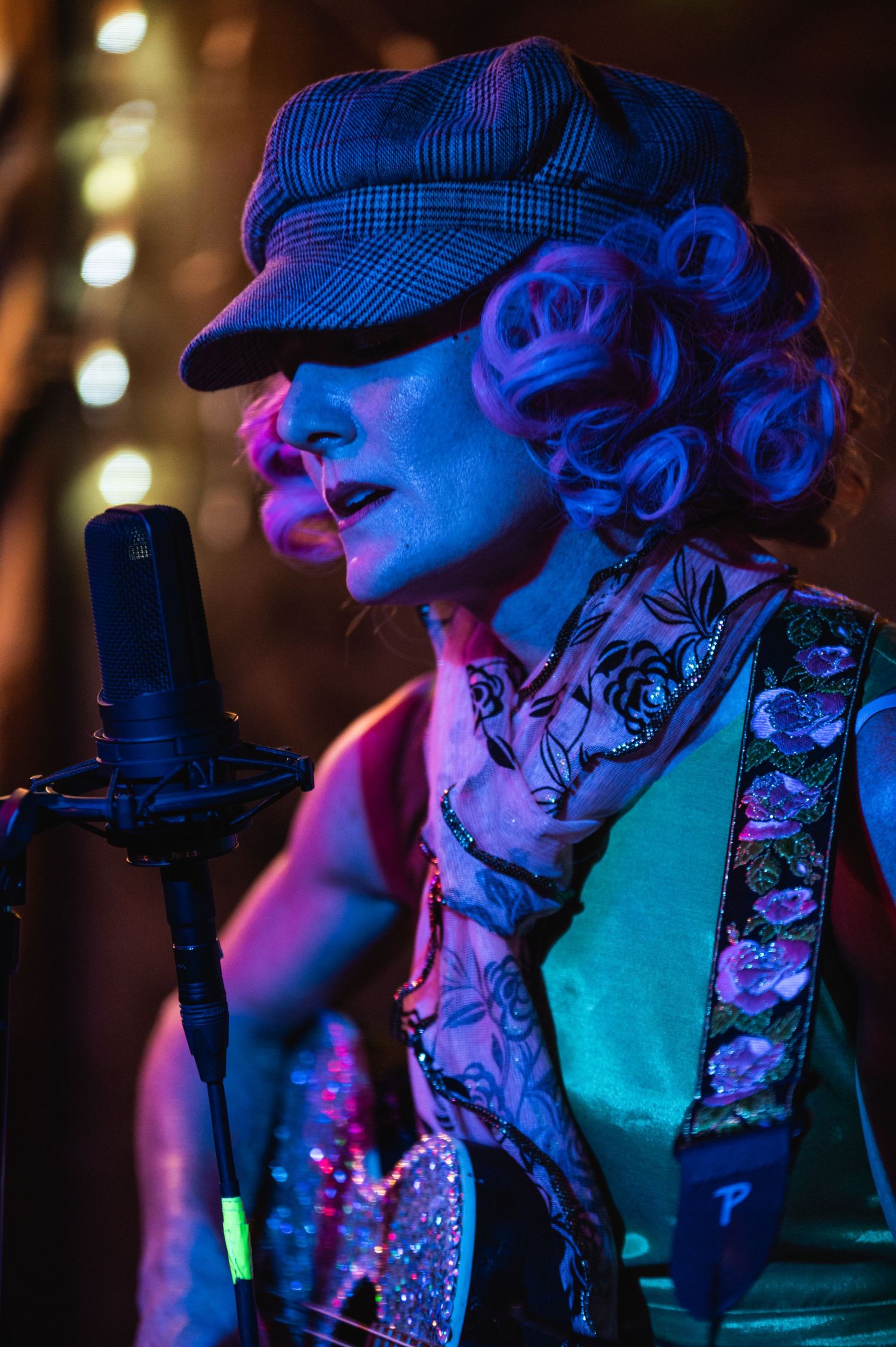 A musician in a cap performs under dramatic blue and purple lighting with a professional microphone.