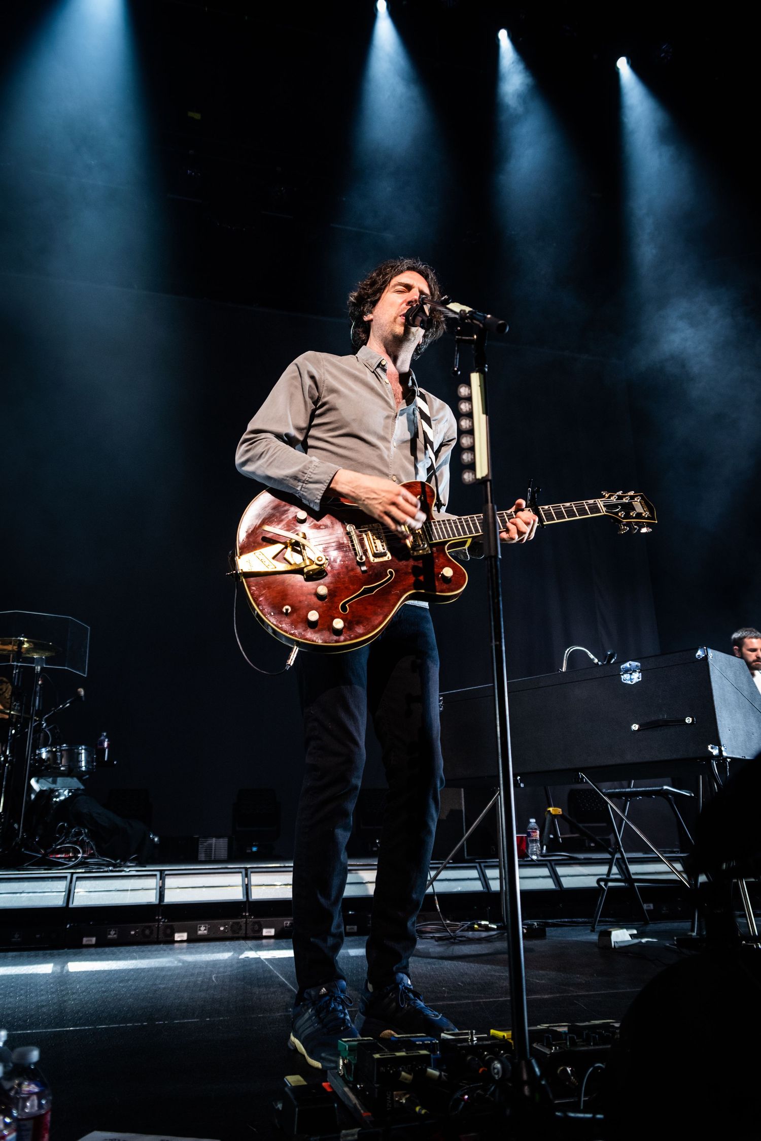 Concert performer plays red hollow body guitar under dramatic blue stage lighting.