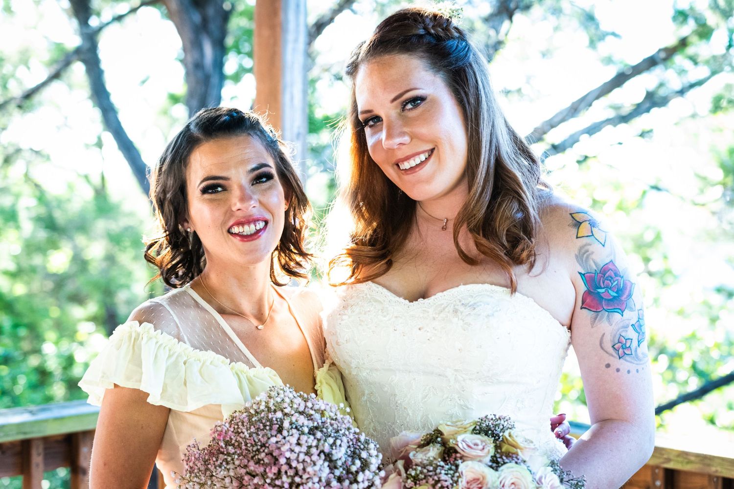 Two wedding attendants pose together holding bouquets and wearing light-colored dresses.