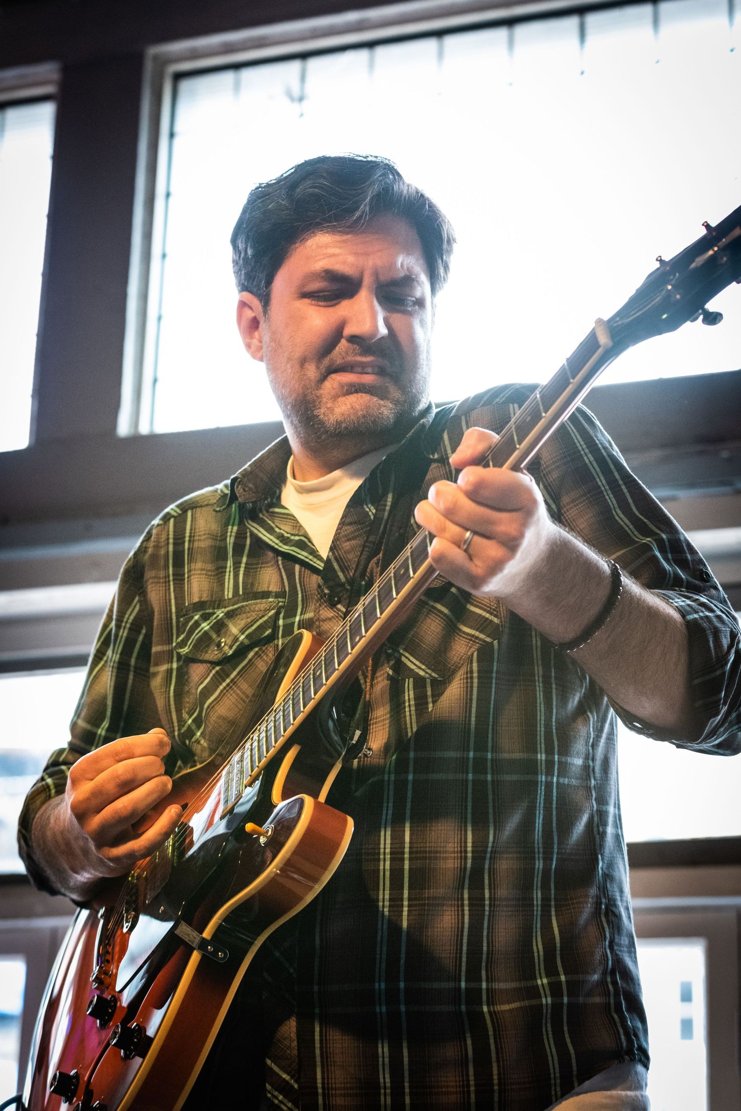 A musician playing an electric guitar while performing in a sunlit venue.