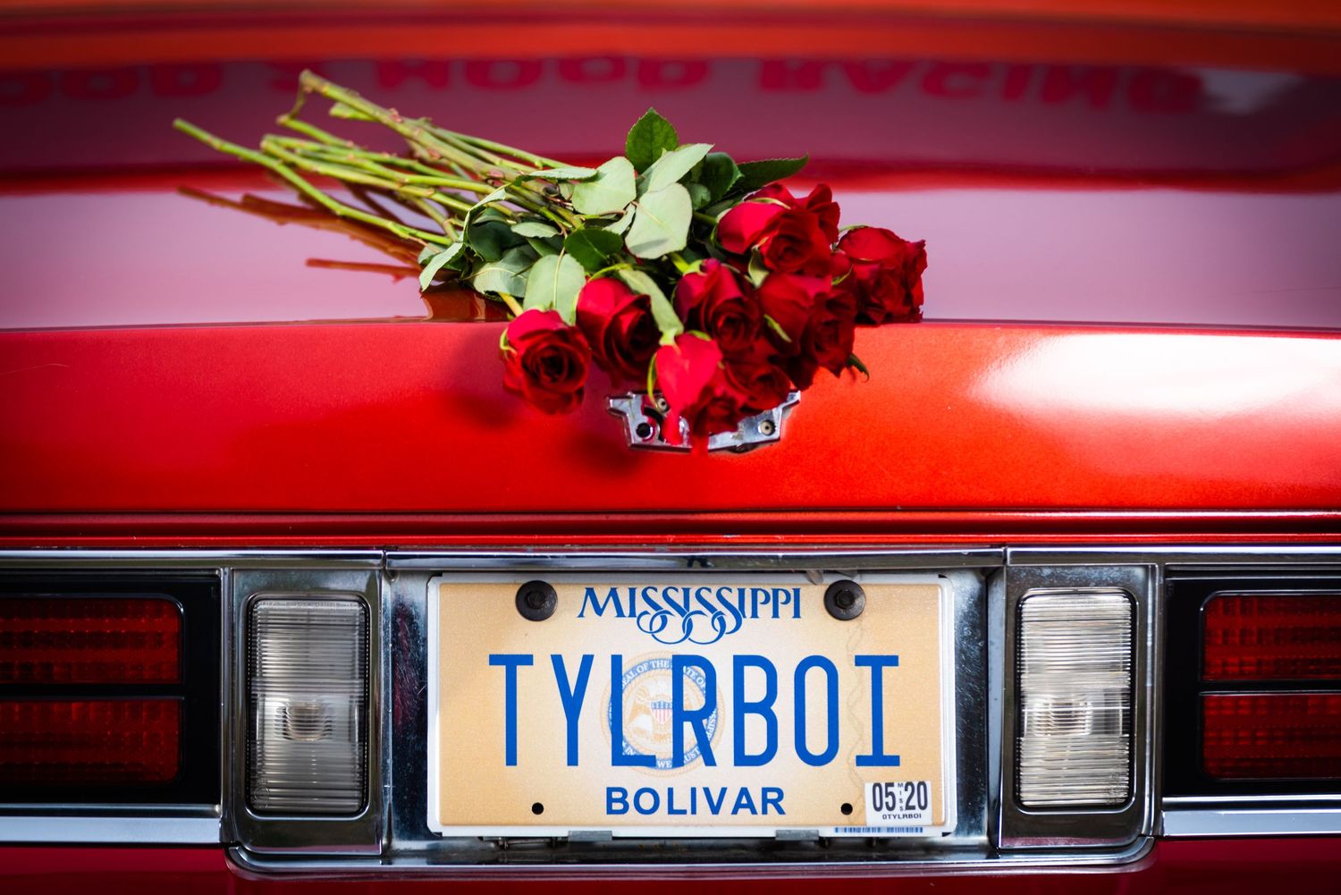 Long-stemmed red roses placed on red car hood above Mississippi TYLRB01 license plate.