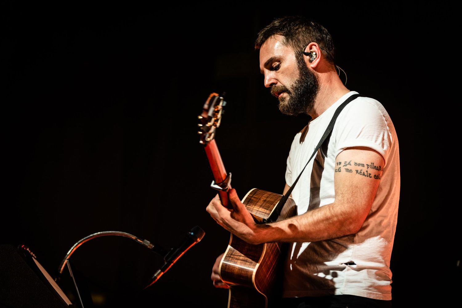 Musician in white shirt playing acoustic guitar against black background during performance.