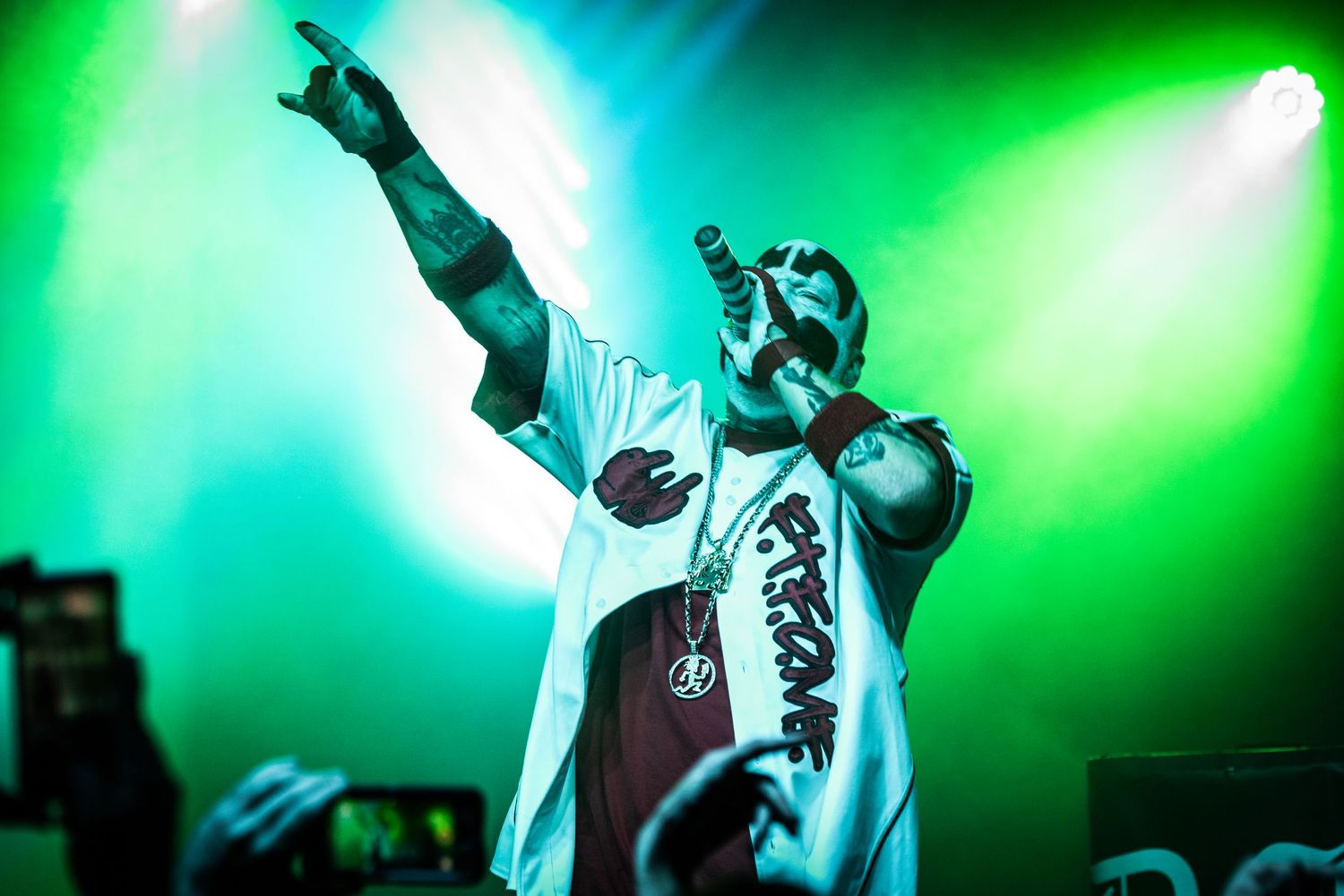 Performer in white costume against vibrant green and blue stage lighting during concert.