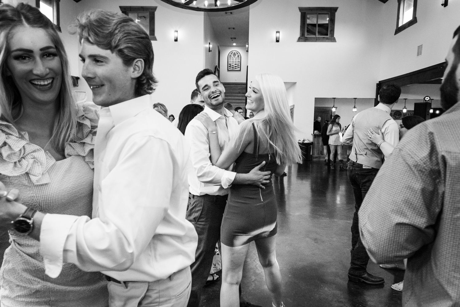 Black and white photo of guests dancing and celebrating at a wedding reception.