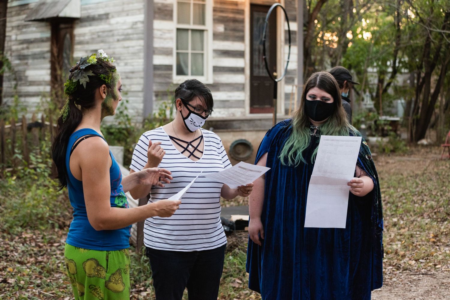 Three people review papers together outdoors while wearing masks during autumn.