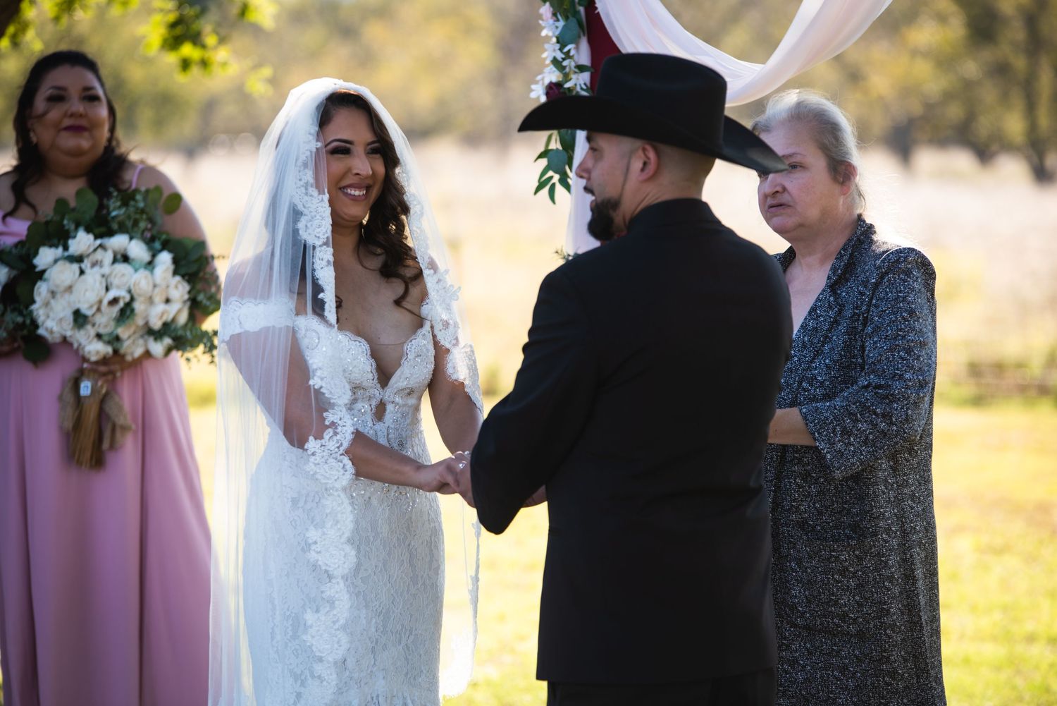 Outdoor wedding ceremony with floral arrangements and attendants in pink dresses.
