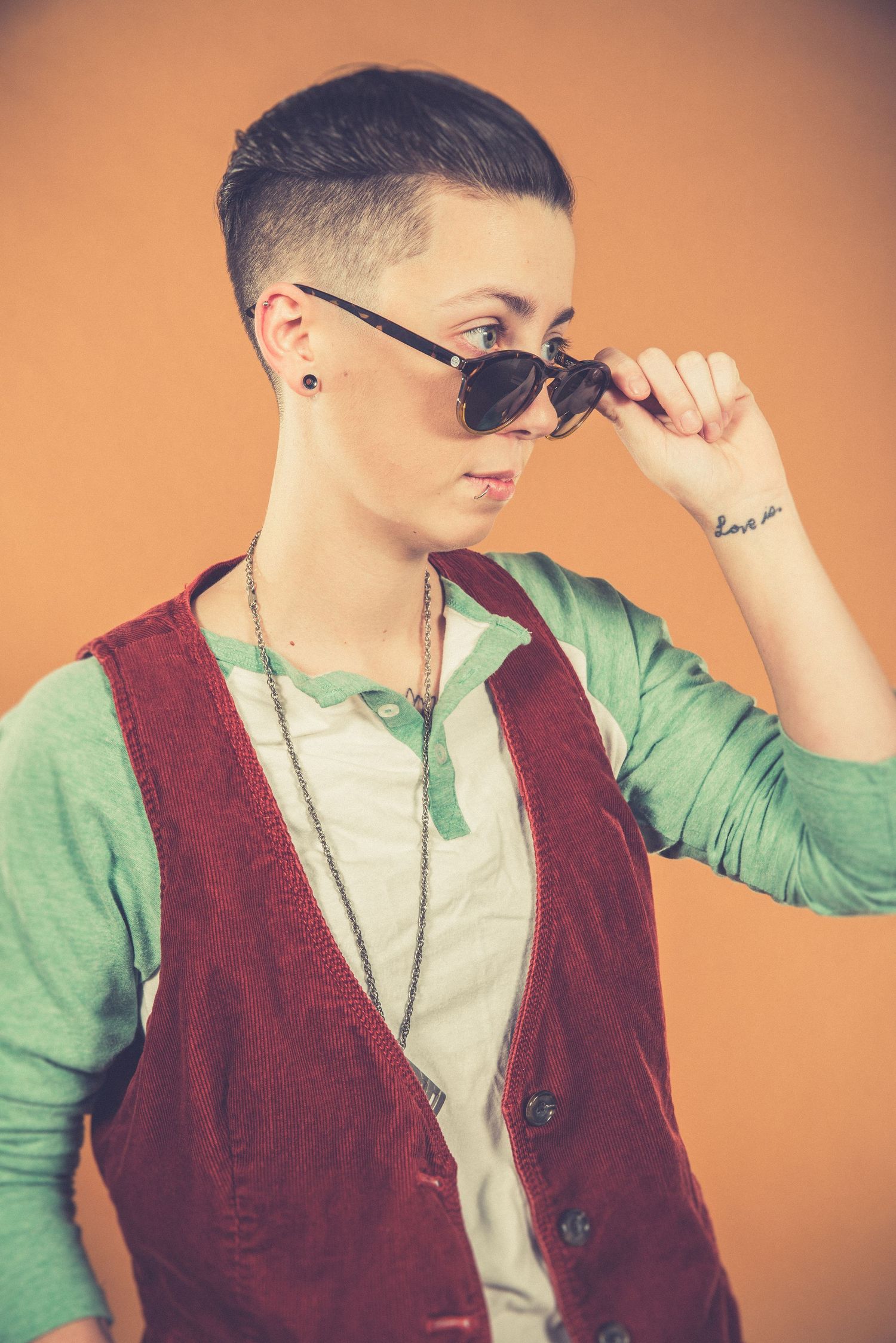 Cool portrait of person in burgundy vest and mint shirt adjusting sunglasses.