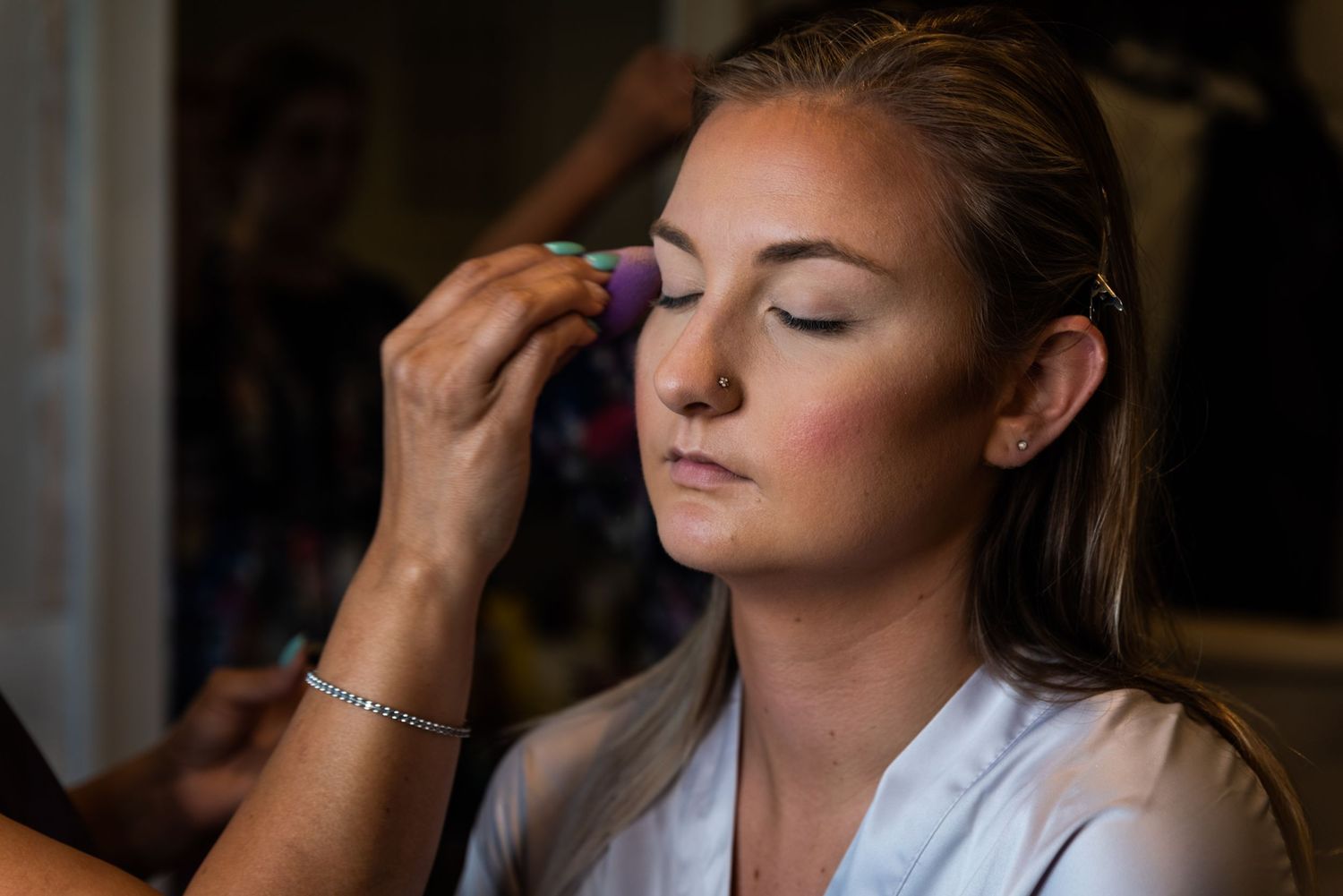 Makeup artist applies eyeshadow during professional beauty preparation session in soft lighting.
