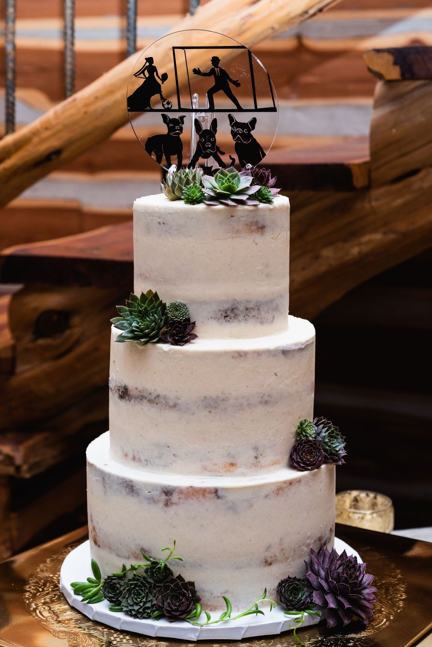 Three-tiered semi-naked wedding cake decorated with succulents and a silhouette skiing topper.