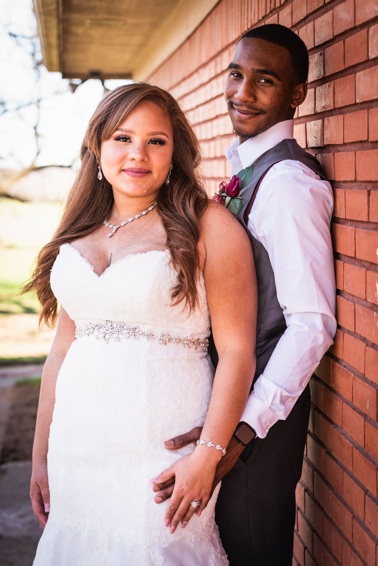 Intimate portrait of bride in beaded wedding dress with groom in vest against brick backdrop.