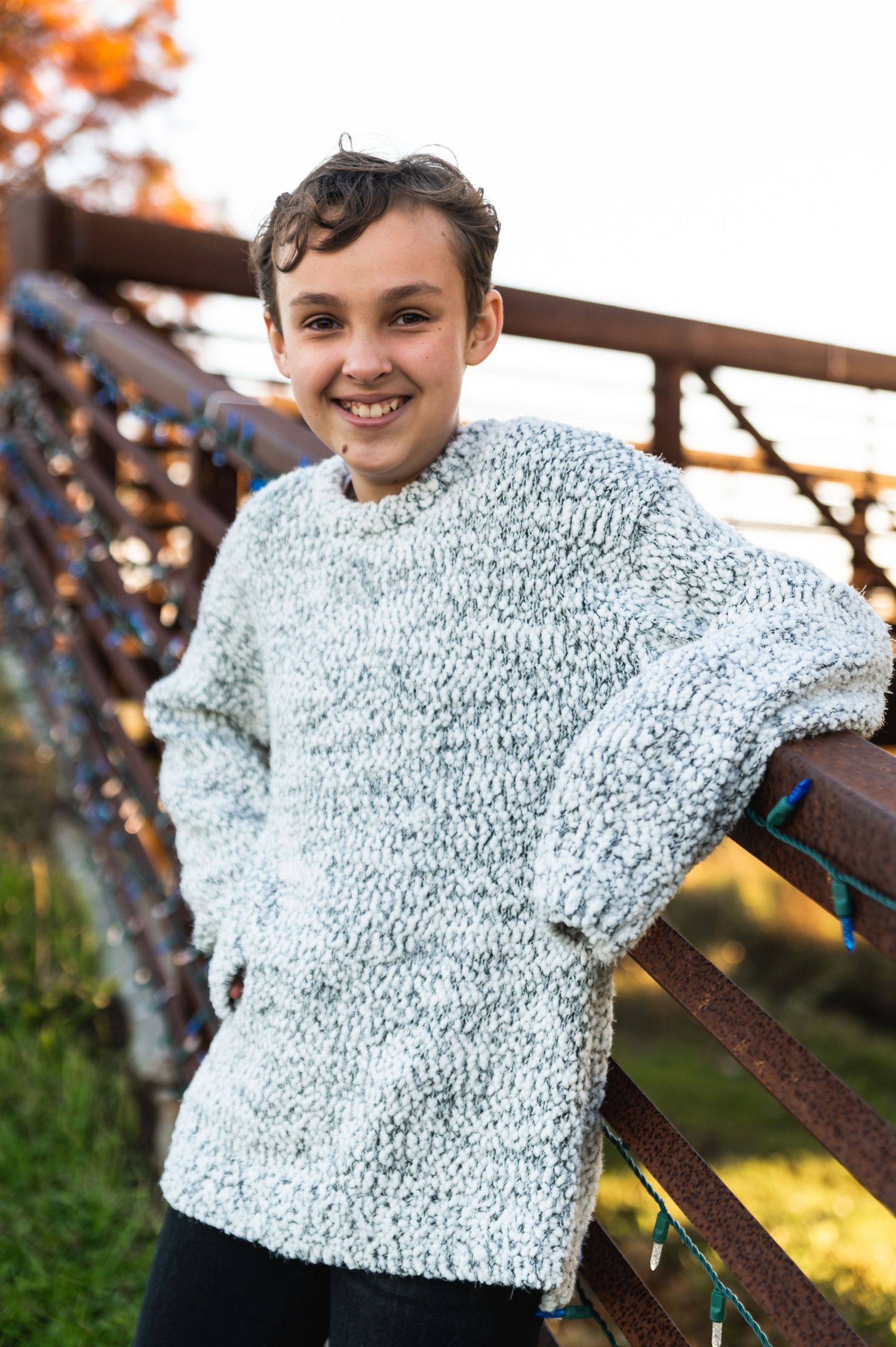 Person in chunky knit sweater posing by rustic railing during autumn sunset.
