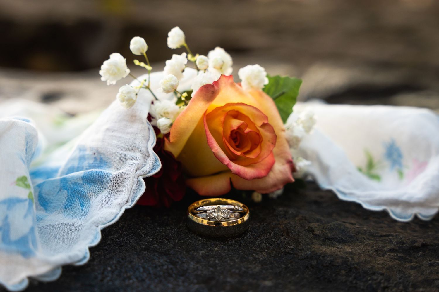 Wedding ring with peach rose and white flowers on lace handkerchief.