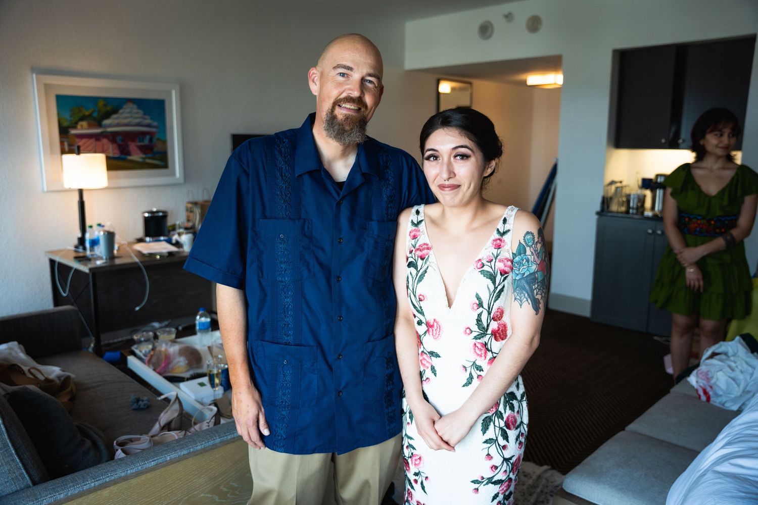 Couple stands together in casual attire inside bright hotel room.
