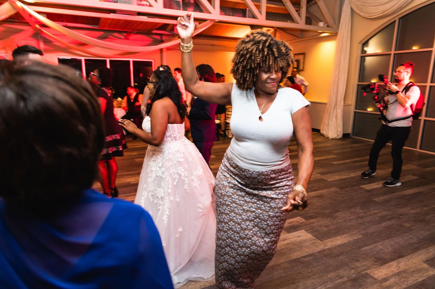 Wedding guests dancing and celebrating on a hardwood floor under decorative beams.