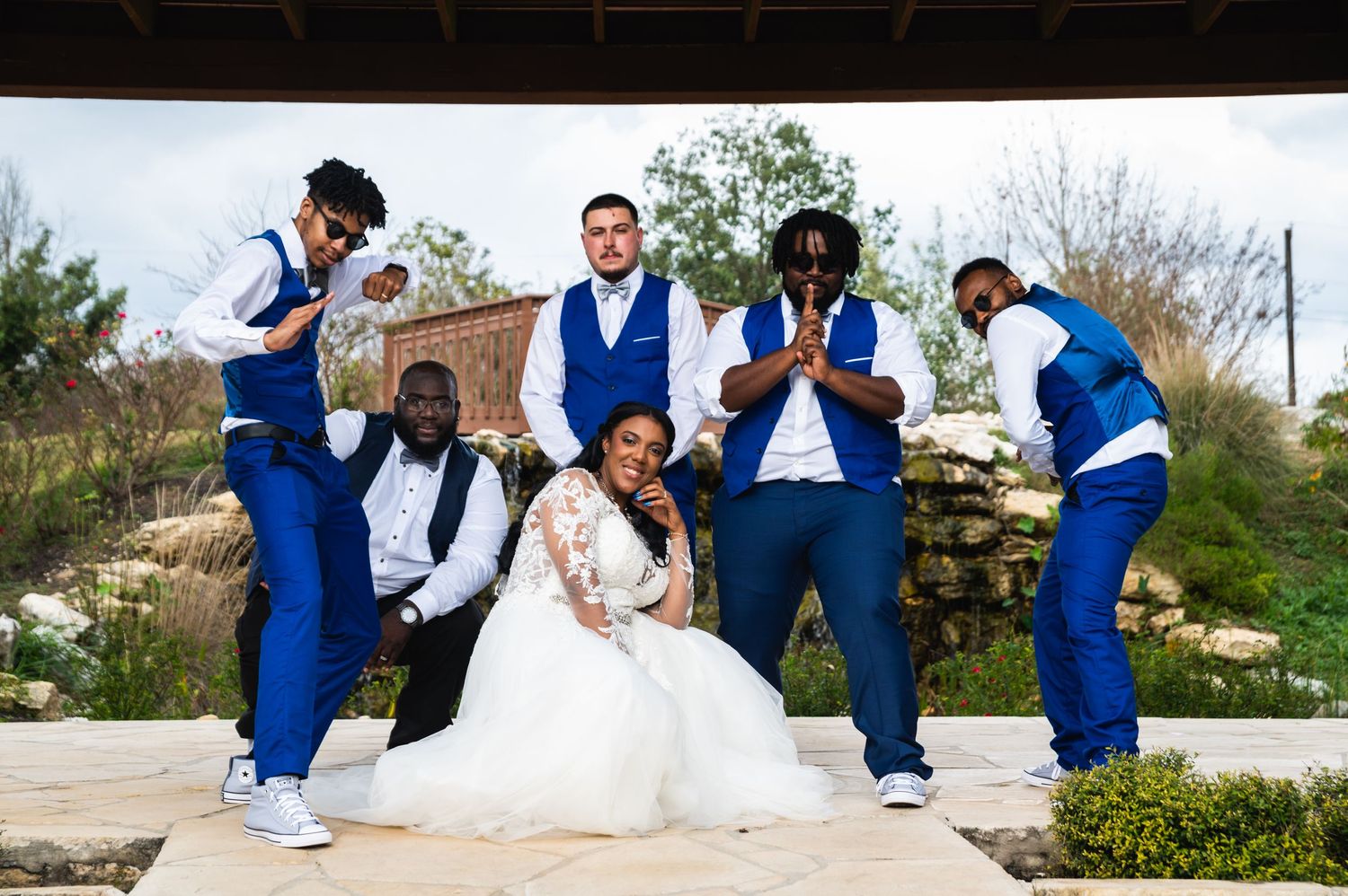 Wedding party strikes fun poses on outdoor stone pathway wearing coordinated blue and white attire.