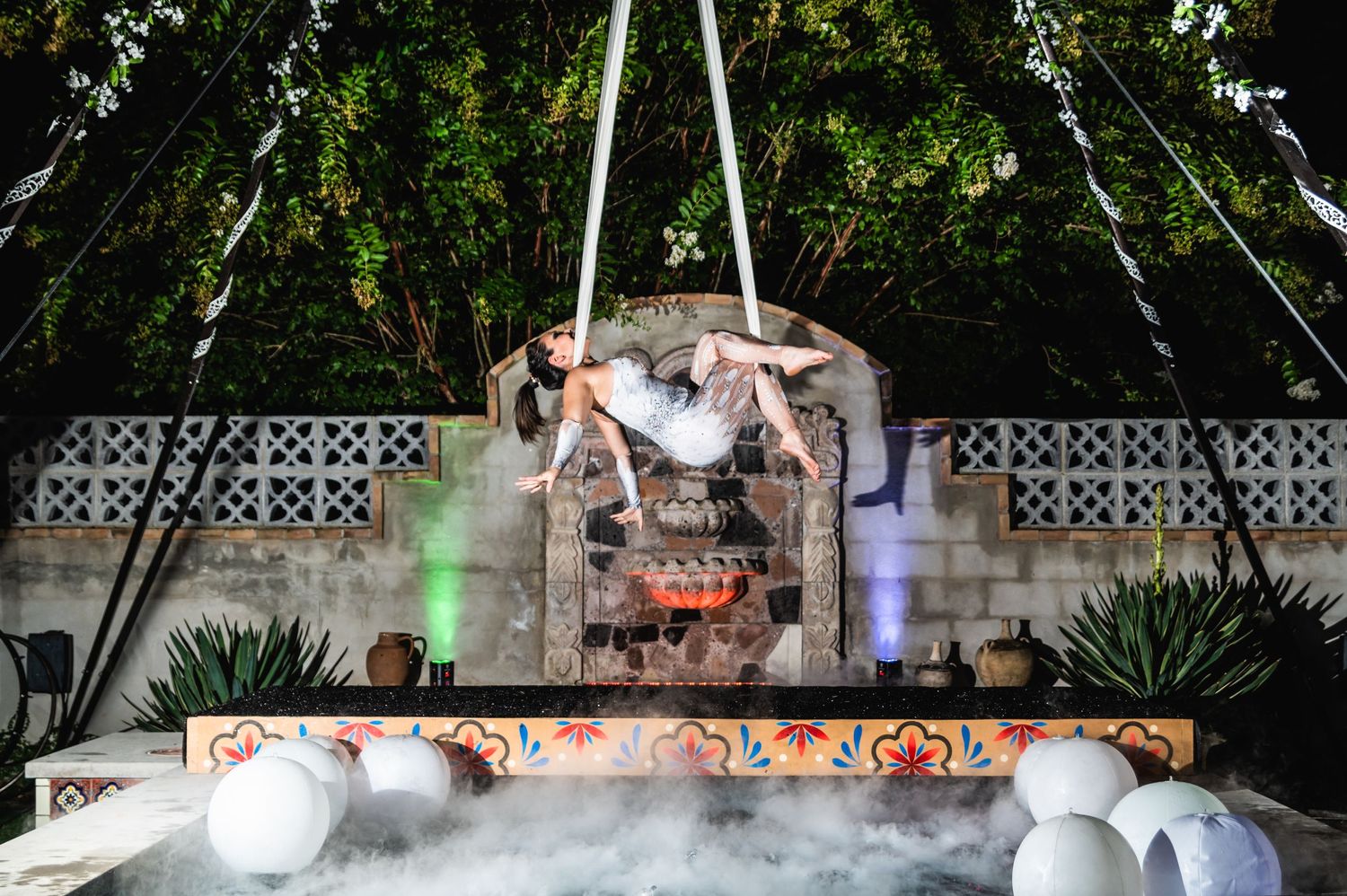 Aerial performer executing a dramatic pose above a misty stage with white balloons and greenery decorations.