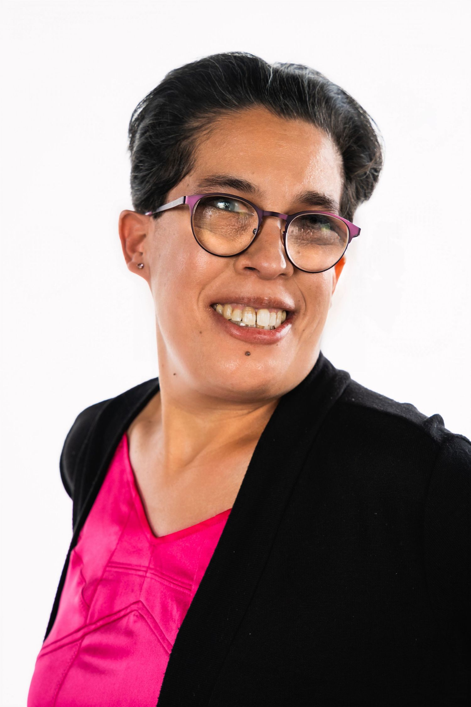 Professional wearing glasses and black blazer with pink top in studio portrait.