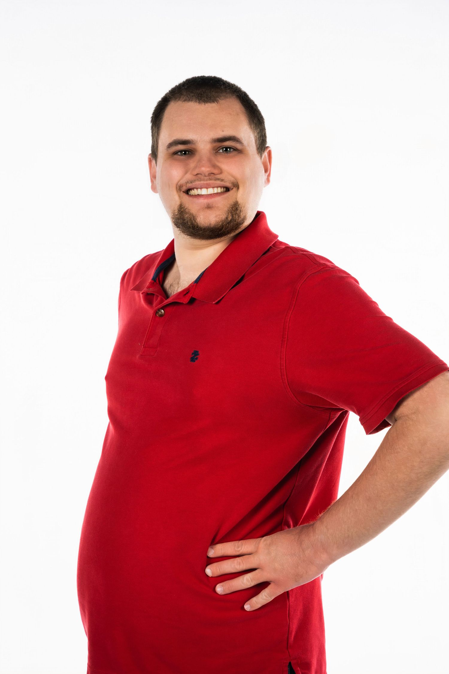 Studio portrait of someone in red polo shirt with hand on hip against white background.