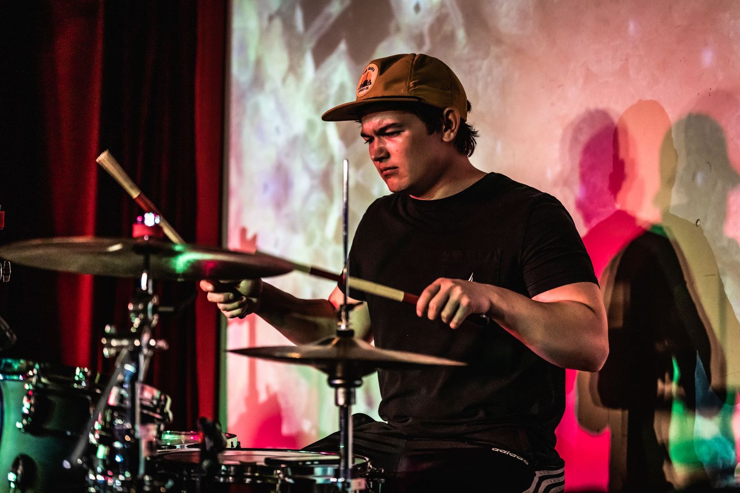 Drummer performing on stage with colorful lighting and projections in the background.