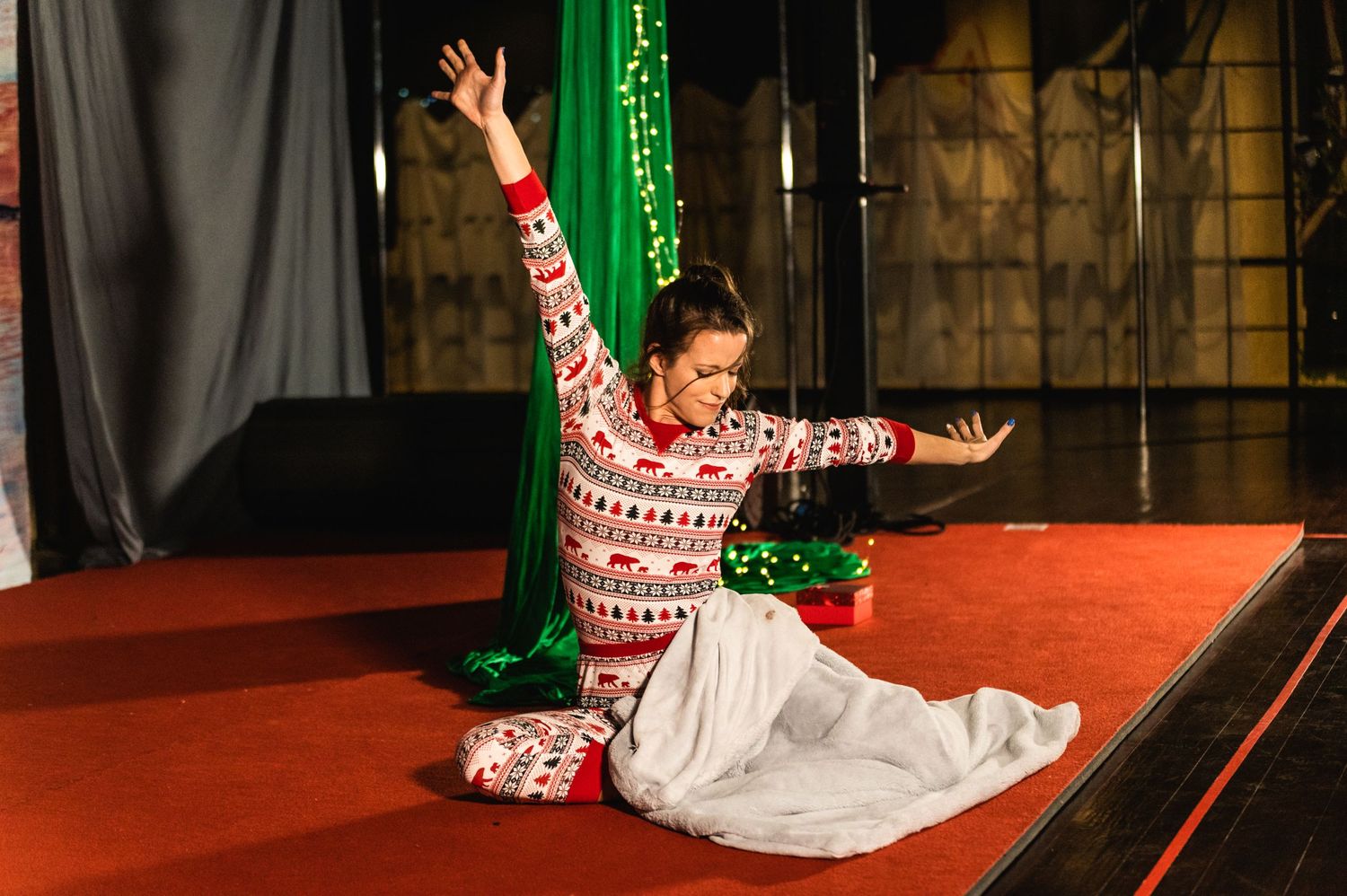 A dancer in a festive sweater and white skirt performs on a red stage with green accents.