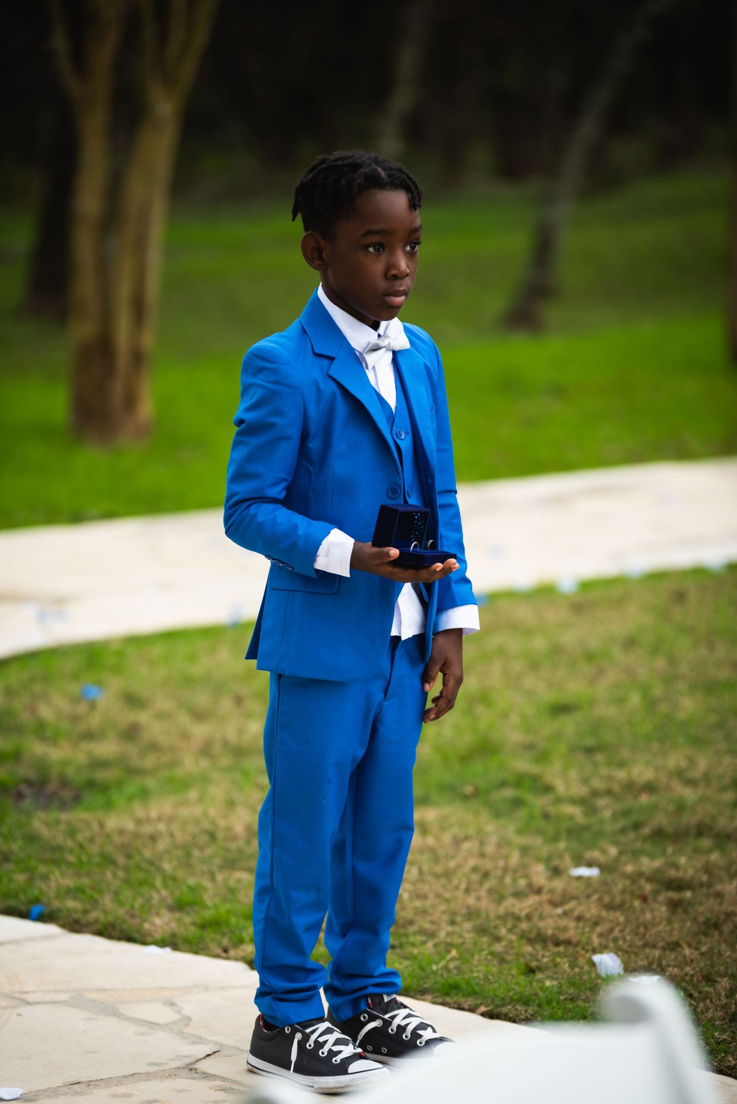 Young attendant in bright blue suit and white tie stands on garden path.