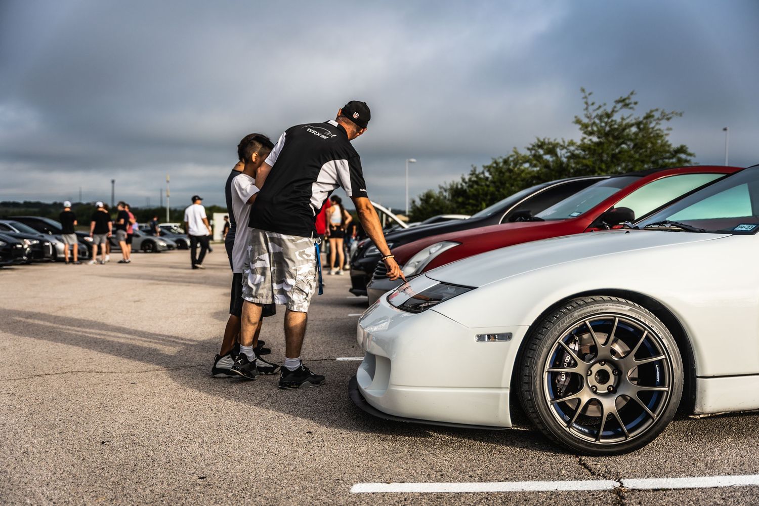 Car enthusiasts admiring modified vehicles at outdoor automotive gathering.