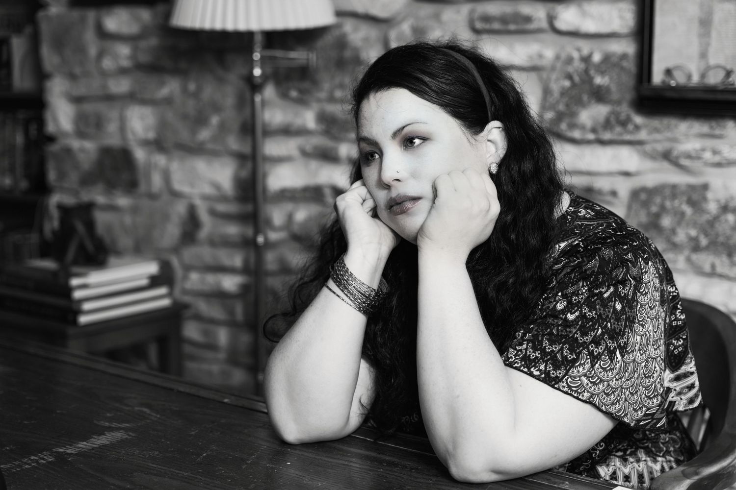 Portrait of woman with dark hair in vintage setting with stone wall background.