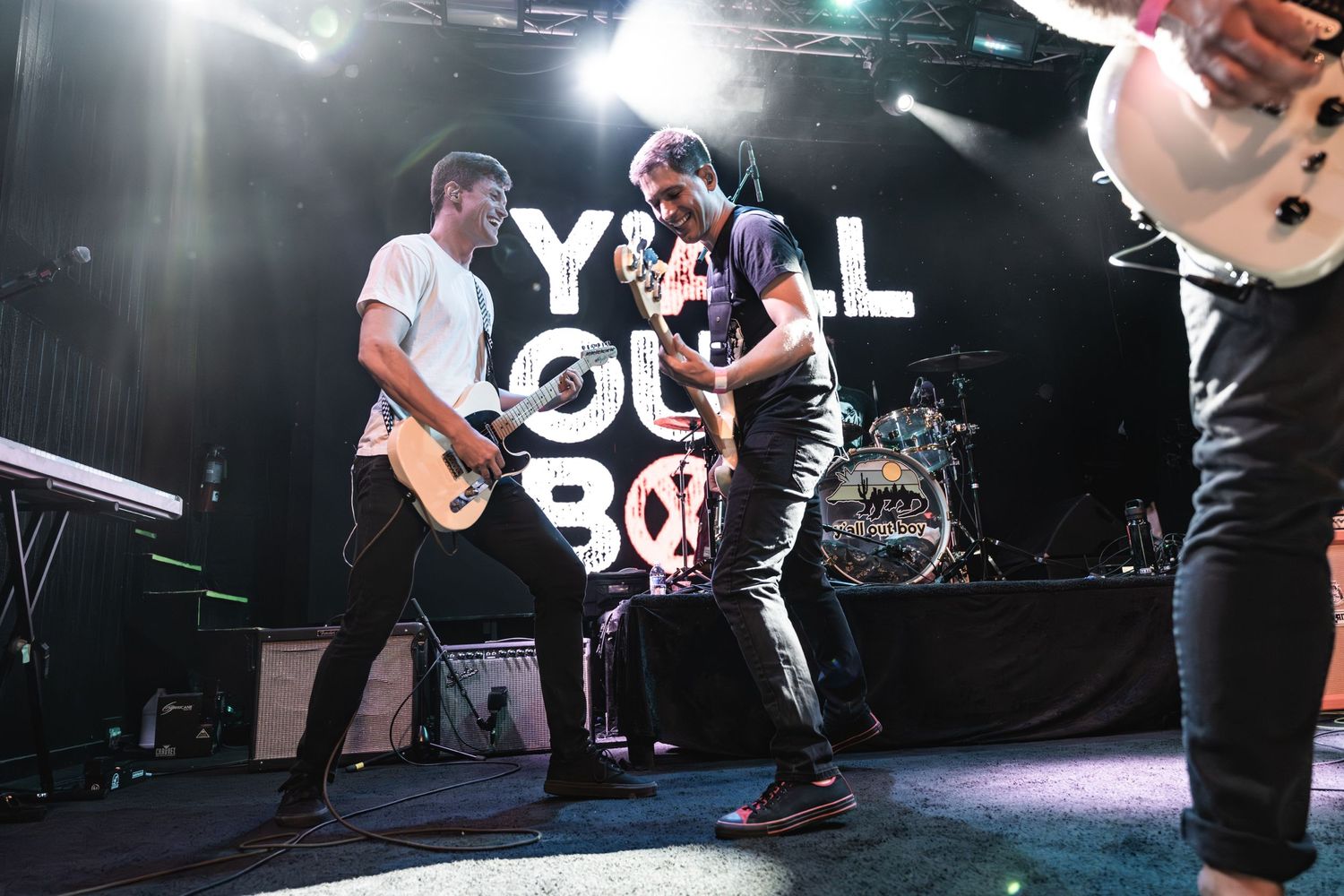 Energetic performance on stage with musicians playing guitars in front of a large logo backdrop during a live show.