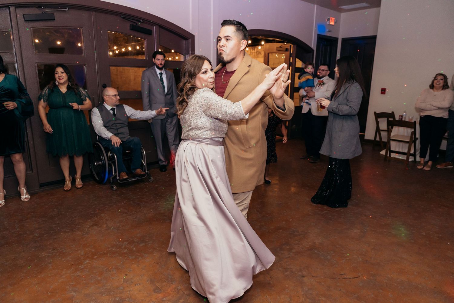 Dancers in formal attire perform a romantic dance at an indoor wedding reception with string lights.