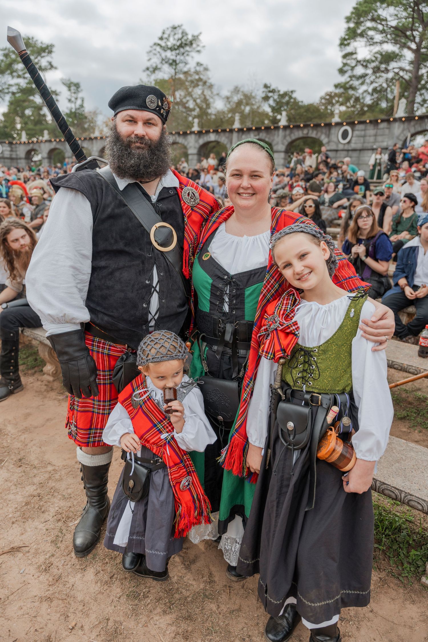 Family in traditional Scottish and renaissance faire attire posing at an outdoor festival.