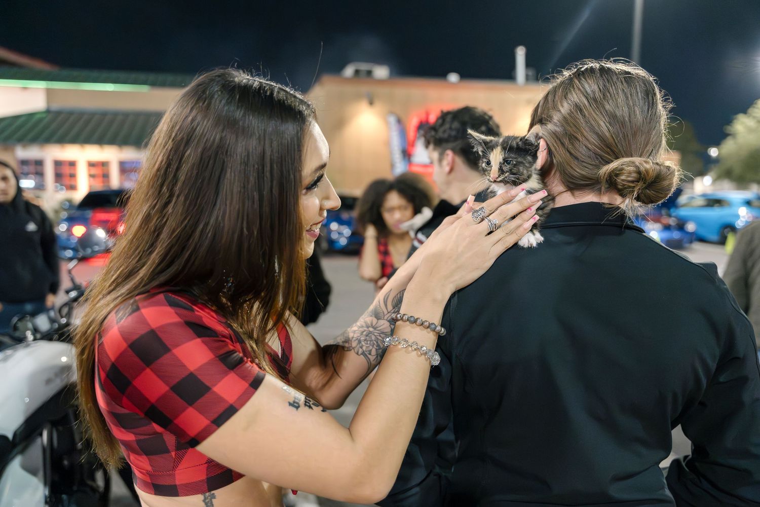 Friends sharing a moment with a cat at a nighttime car meetup.