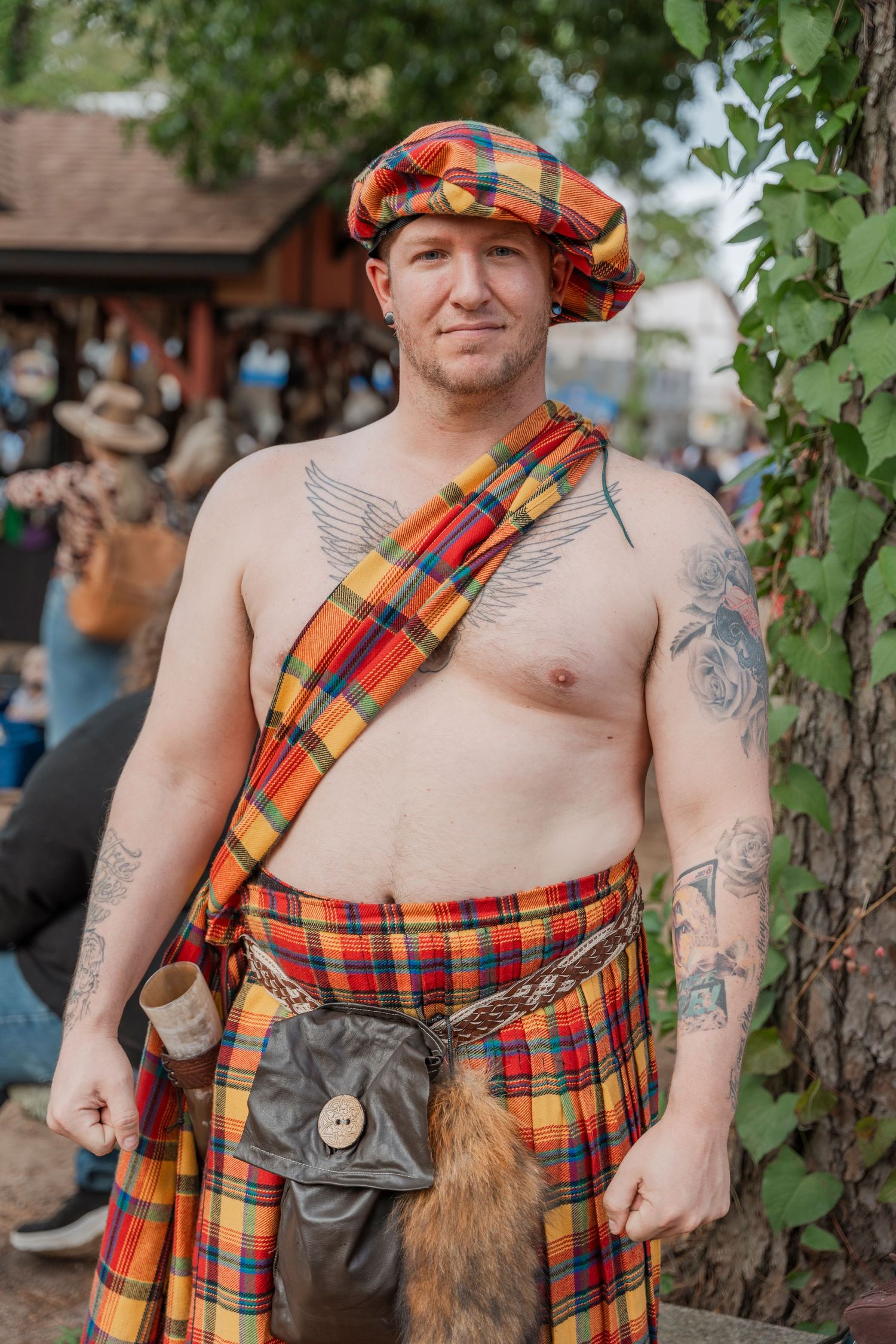 A performer wearing traditional Scottish highland dress with plaid kilt and sash at a festival.