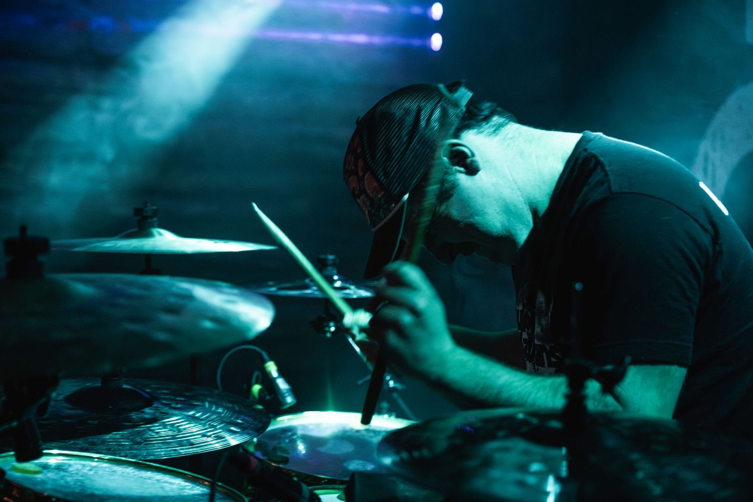 Drummer performing in moody blue stage lighting during live concert.