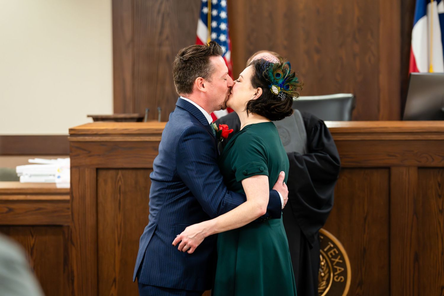 A couple shares a kiss in a courthouse during what appears to be a wedding ceremony.